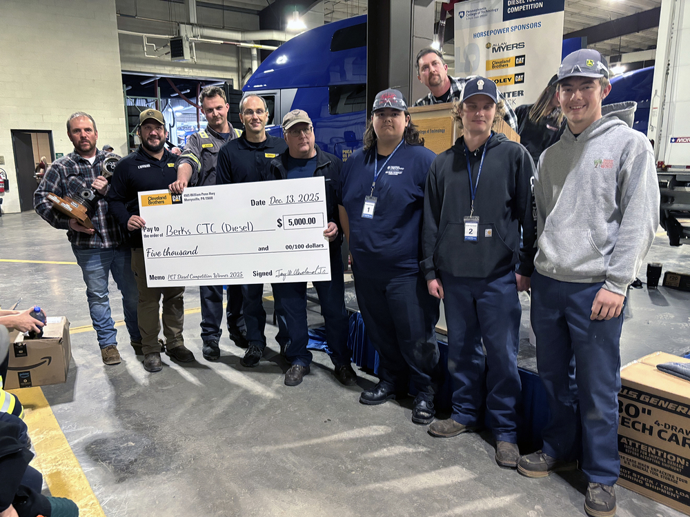 A group of Diesel Technology students, instructors, and industry representatives stand inside a diesel training facility holding a large ceremonial check for $5,000 made out to Berks Career & Technology Center Diesel. A semi-truck and competition signage are visible in the background, marking the award presentation following a diesel technology competition.