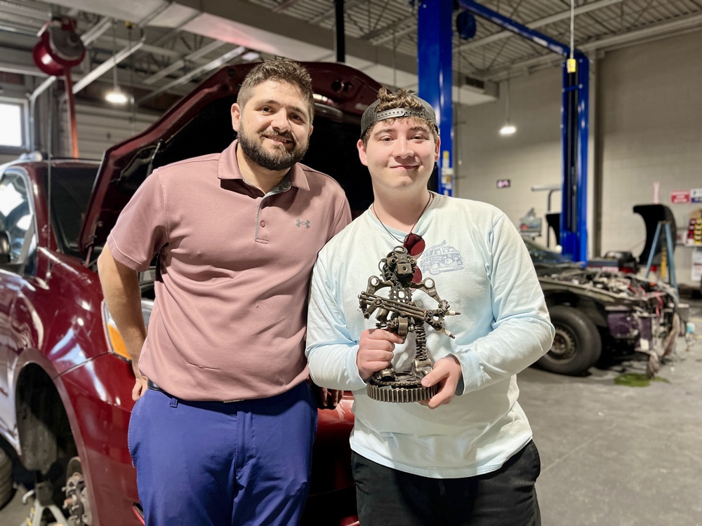 Automotive Technology instructor Dustin Mauger stands with student Ryan Kraft, who is holding a custom trophy made from automotive parts in the BCTC shop.