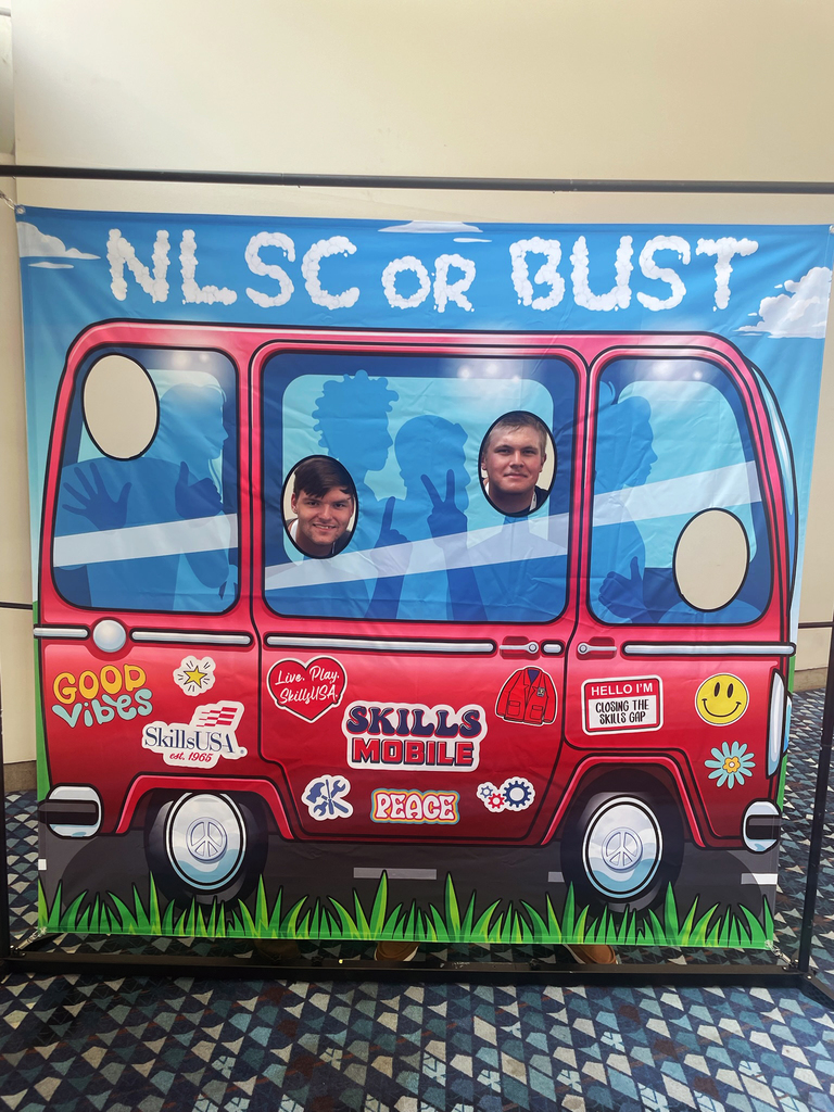 A colorful backdrop designed to resemble a red van with various stickers and decorations. The top of the backdrop reads 'NLSC OR BUST.' There are cutouts in the van's windows for people to place their faces. Stickers on the van include phrases such as 'Good Vibes,' 'SkillsUSA,' 'Live, Play, SkillsUSA!,' 'SKILLS MOBILE,' 'PEACE,' and a name tag that says, 'HELLO I'M GOING TO THE NLSC OR BUST.