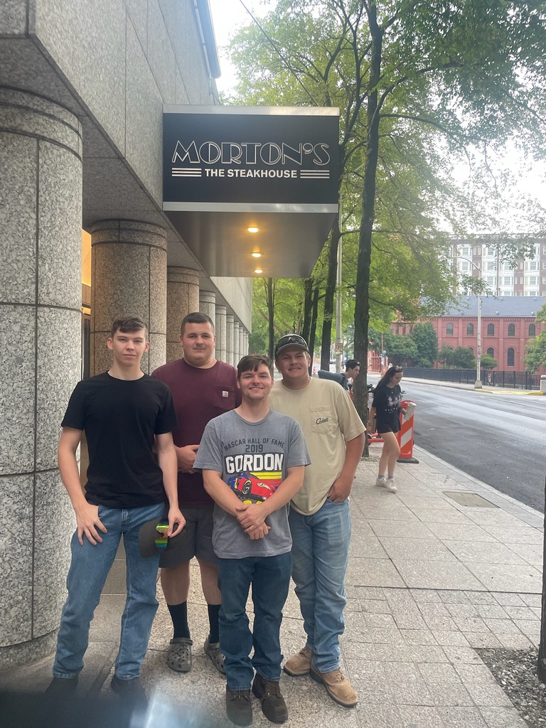 Four individuals stand on a sidewalk in front of Morton's The Steakhouse.
