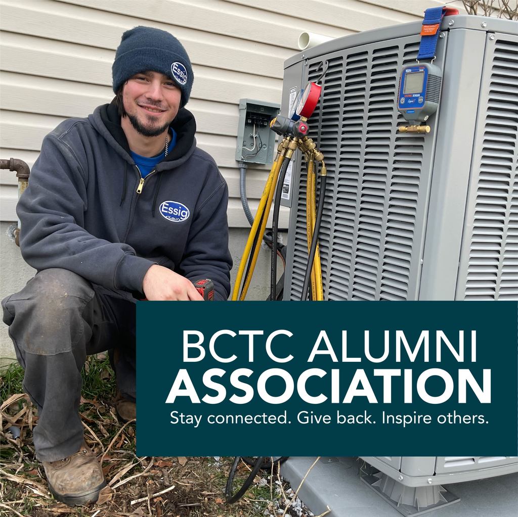 A person wearing a dark hoodie with an "Essig" logo and a beanie is crouching next to an outdoor air conditioning unit. The unit has several hoses and gauges attached. In the foreground, a green banner with white text reads: "BCTC Alumni Association. Stay connected. Give back. Inspire others." The background features the beige siding of a house.