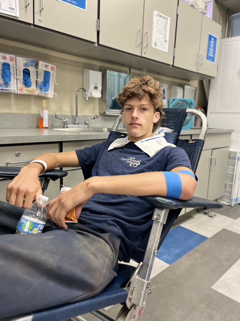 A BCTC student relaxes in a donation chair with a blue bandage on his arm after giving blood. He holds a water bottle and snack bag.