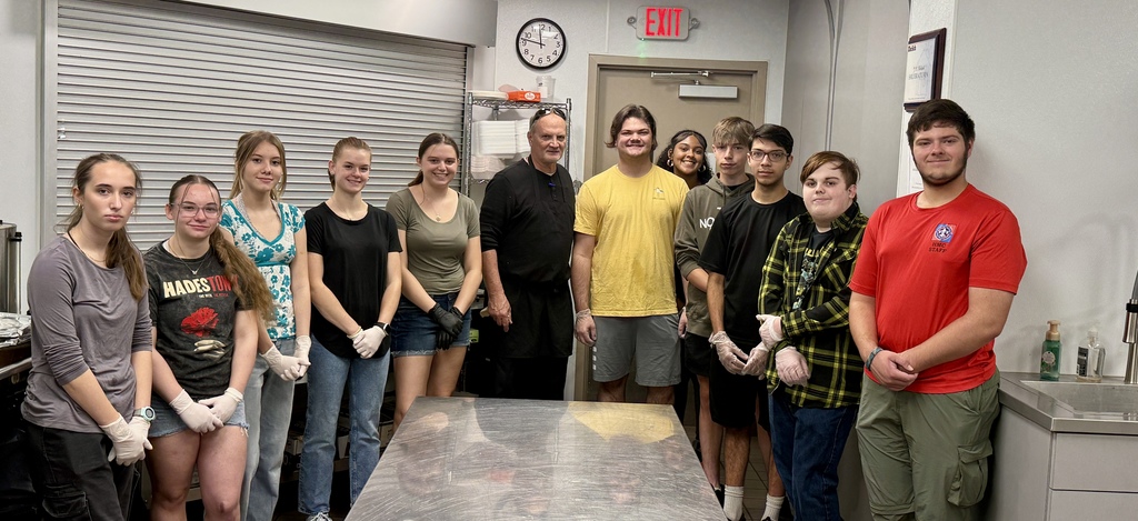 A group of eleven students and an instructor pose together in the kitchen, smiling proudly after completing their volunteer service.