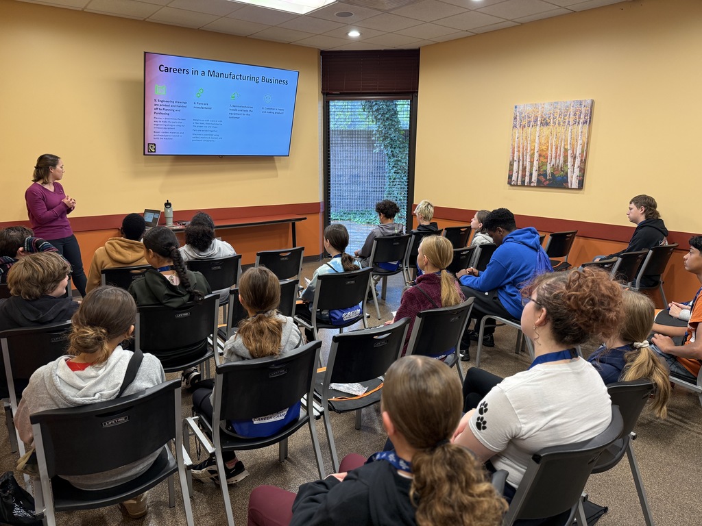 A classroom of middle school students sits facing a screen labeled "Careers in a Manufacturing Business." A presenter from Reading Truck stands at the front, discussing job roles in manufacturing. Students listen attentively.