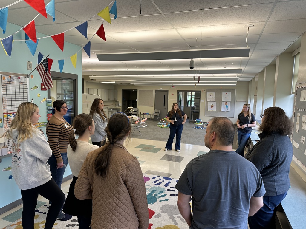 Visitors stand in a bright classroom within the Early Childhood Education program. The room is decorated with colorful flags and children’s learning materials as instructors explain program details.