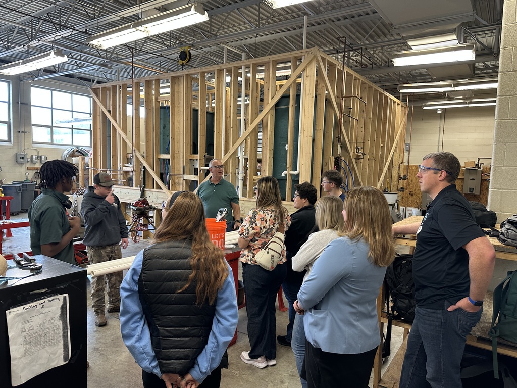CTC Plumbing & Heating students and instructors demonstrate pipe threading equipment to visiting educators inside a workshop setting with wood framing and tools around.