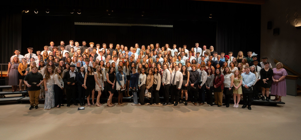 A large group of 231 Berks Career & Technology Center students and staff gather on stage for a group photo during the National Technical Honor Society Induction Ceremony. The students are dressed in professional attire and smiling toward the camera.