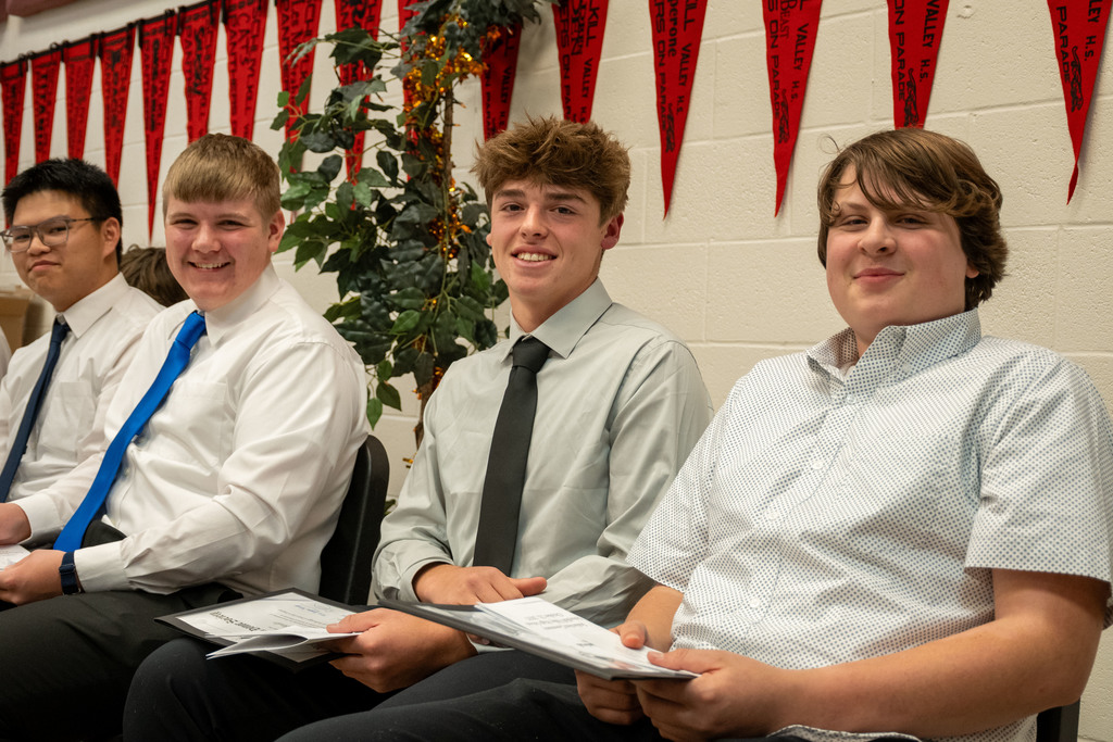 Four male students dressed in white shirts, ties, and dress pants sit in a row holding their National Technical Honor Society certificates, smiling before the induction ceremony at Berks Career & Technology Center.