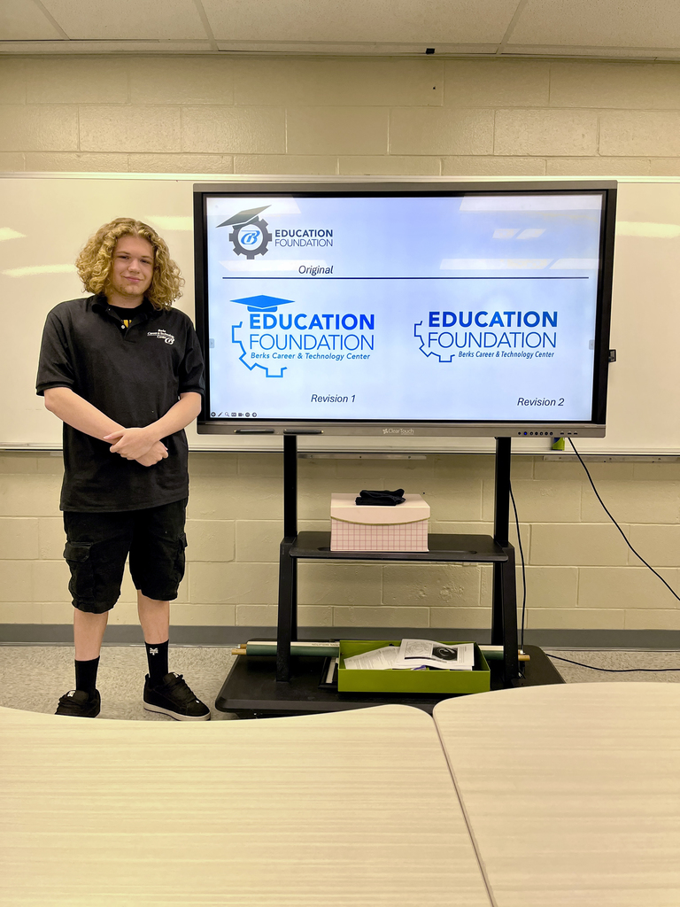 A student stands beside a screen showing the original and revised Education Foundation logo concepts featuring a graduation cap and gear icon. Tables are visible in the foreground.