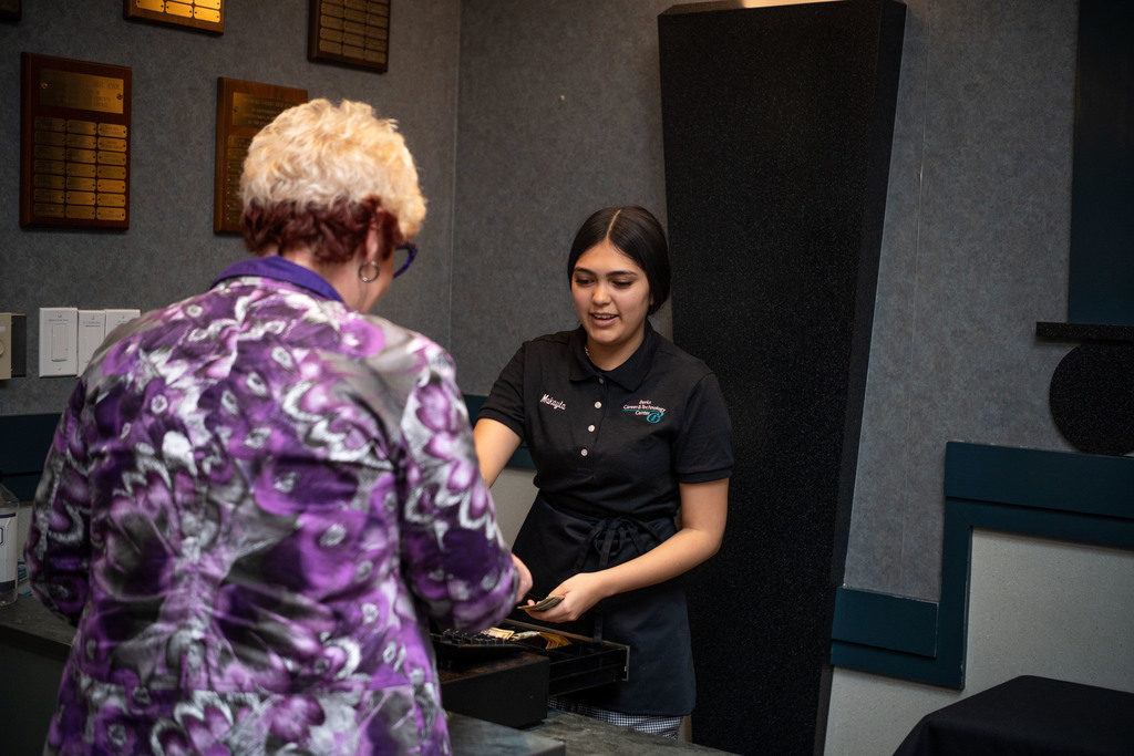 A Hospitality student in a black uniform takes payment from a guest at a counter inside the BCTC restaurant space.