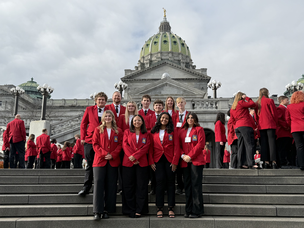 A group of SkillsUSA students and advisors pose on the steps of the Pennsylvania State Capitol. All are wearing red SkillsUSA blazers and black pants. The Capitol’s green dome rises behind them, and additional students in red blazers stand on the surrounding steps.