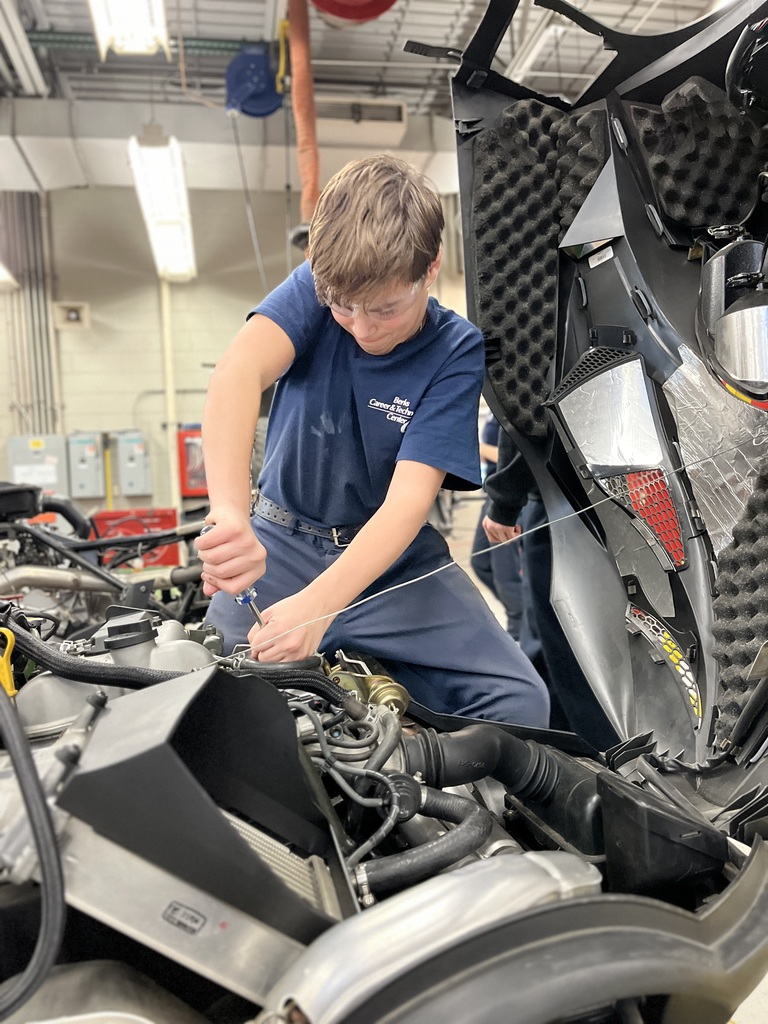 Student wearing safety glasses works inside a snowmobile’s open engine compartment using a hand tool during a recreational vehicle maintenance lesson.
