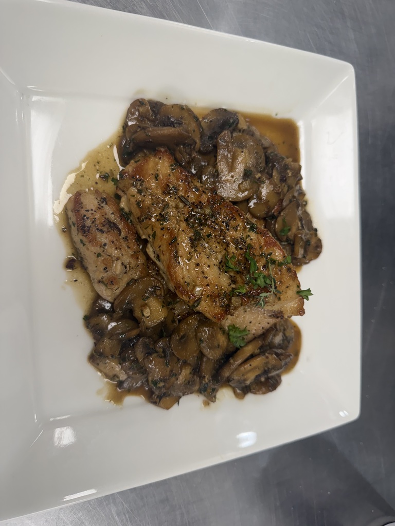 Close-up of plated pork medallions served over sautéed mushrooms with a brown herb sauce in a square white bowl.