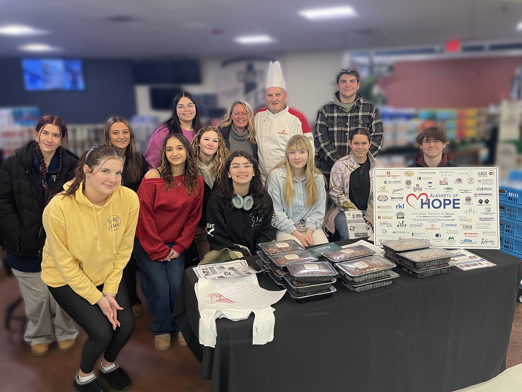Berks Career & Technology Center students and staff stand behind a table displaying packaged chili meals and a “Blankets of Hope” sign during a fundraiser benefiting individuals in need.