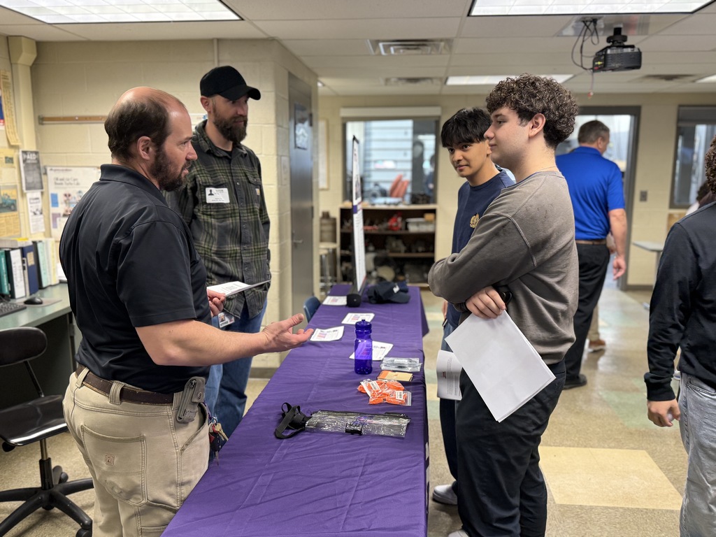 An industry professional speaks with BCTC students at an informational table, answering questions about careers and skills related to construction and transportation fields.