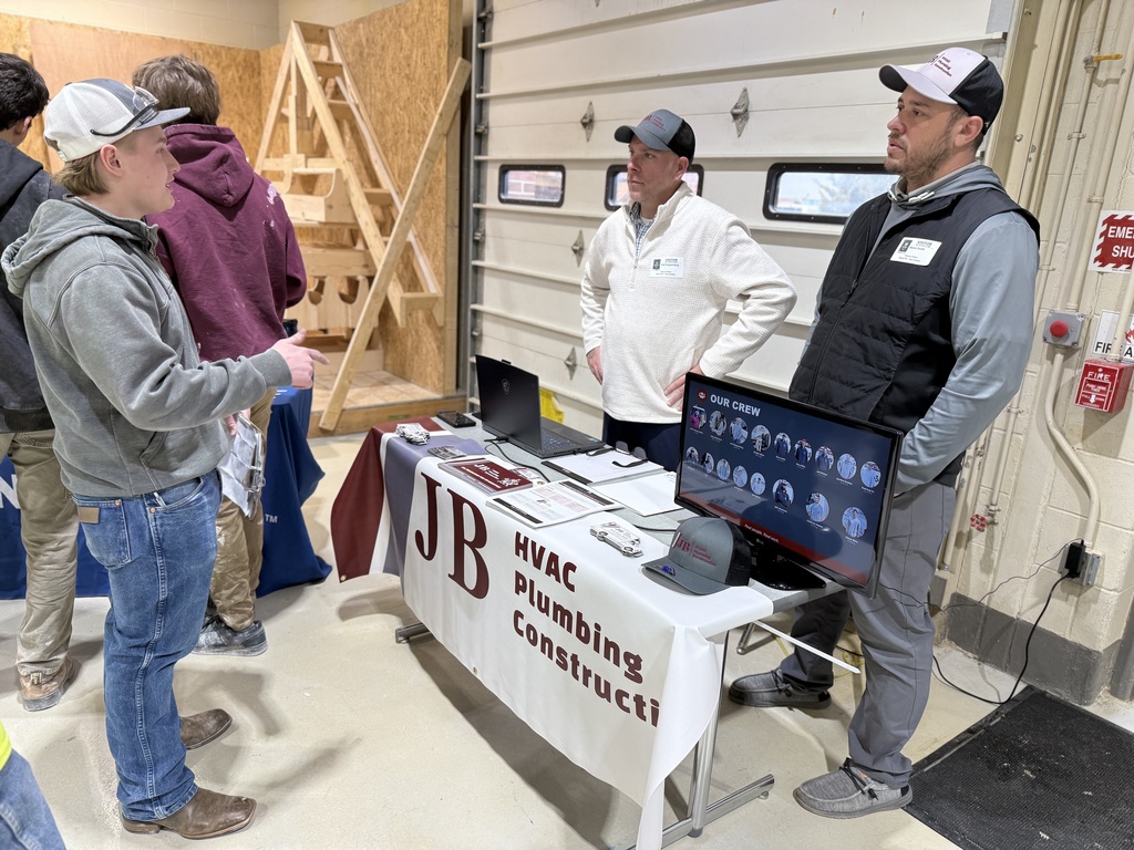 A BCTC student talks with representatives from an HVAC, plumbing, and construction company at an informational table set up inside a construction lab during Career Day.