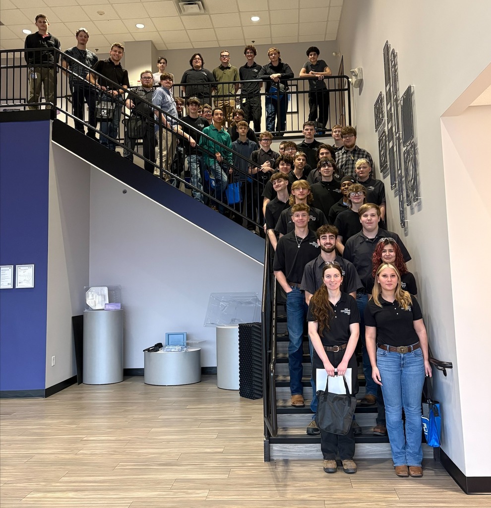 A large group of Berks Career & Technology Center Precision and Computerized Machining Technology students and instructors stand together on a staircase inside a modern manufacturing facility during an industry tour, posing for a group photo.