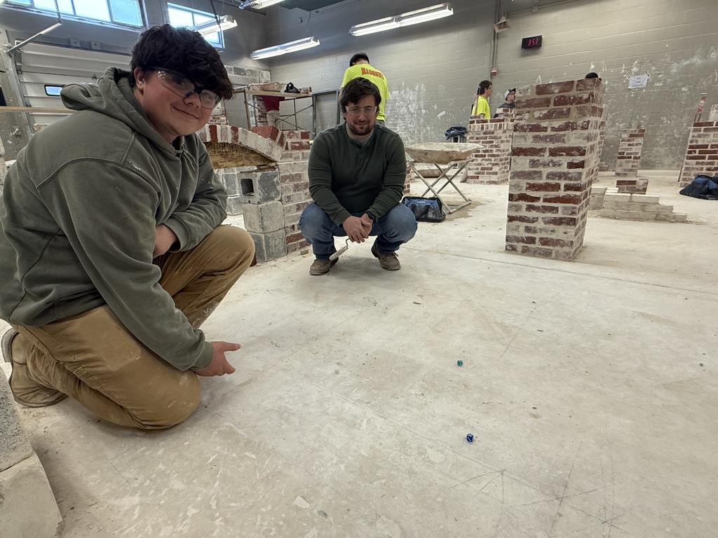 Two masonry students crouch near completed brick columns and arches inside the lab space.