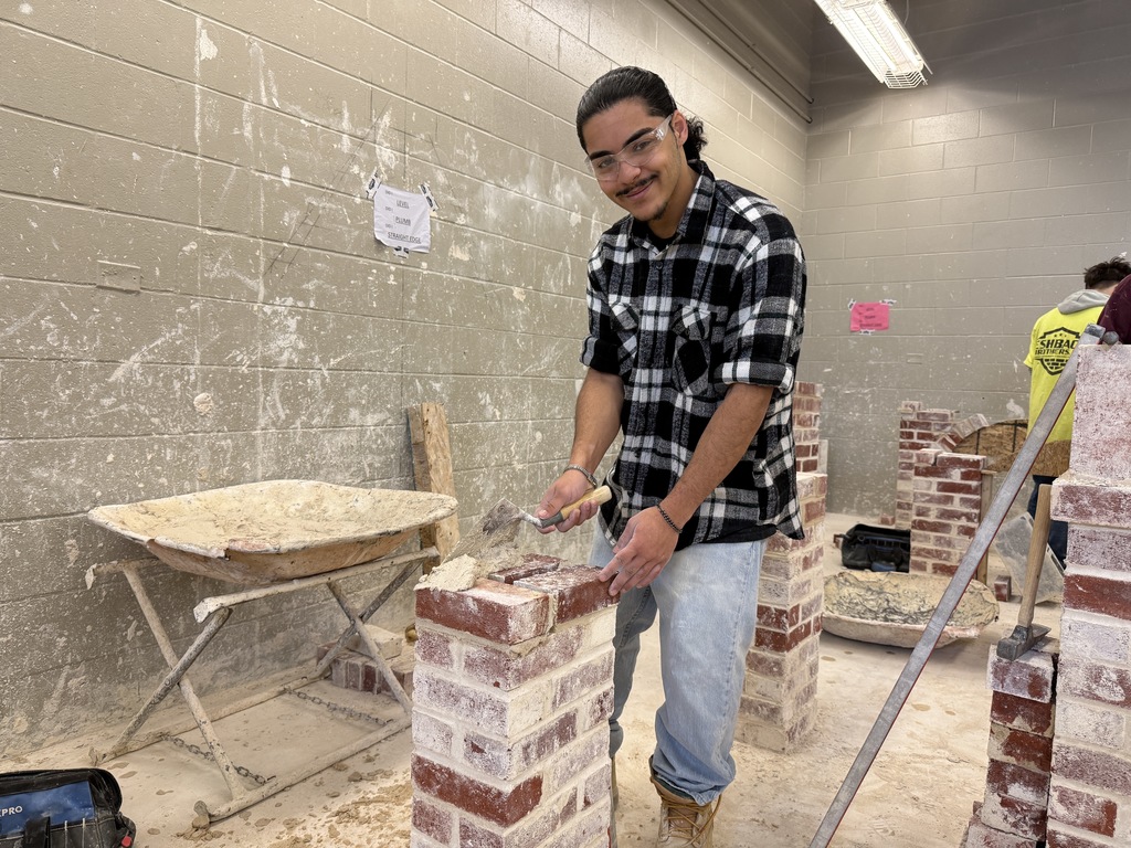 Masonry student spreads mortar on a brick column using a trowel during class instruction.