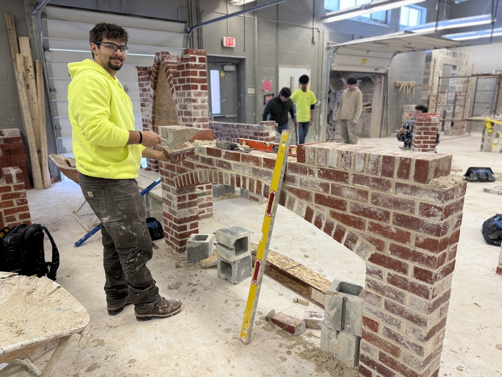 Masonry student applies mortar while building a brick arch structure in a hands-on lab.