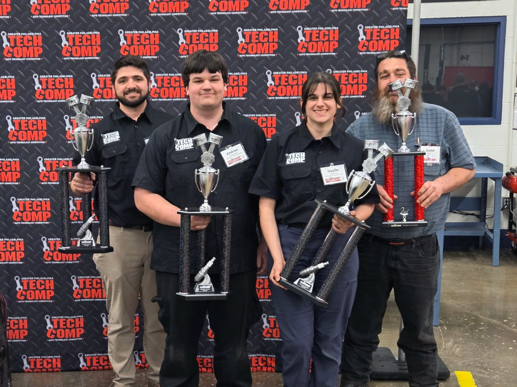 Andrew and Haylie, Automotive Technology students from Boyertown Area Senior High School, stand with their instructor and another competitor while holding trophies in front of a “Greater Philadelphia Tech Comp” backdrop after earning 2nd place.