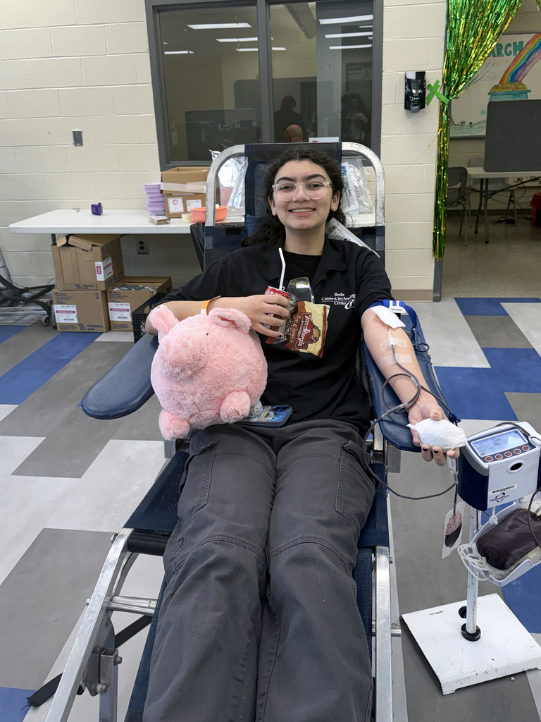 Student donor relaxes in a blood donation chair holding a plush pig and snacks while donating blood at the BCTC blood drive.