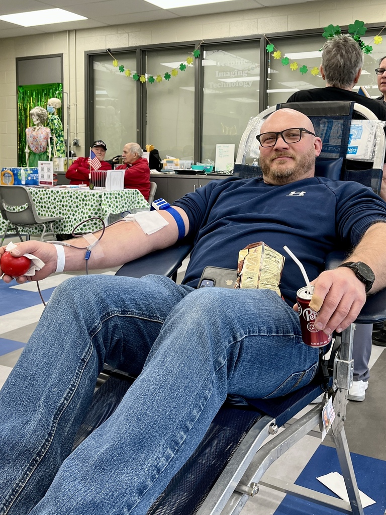 Adult donor relaxes in a reclining chair while giving blood during the St. Patrick’s Day themed blood drive at BCTC, holding a snack and drink.