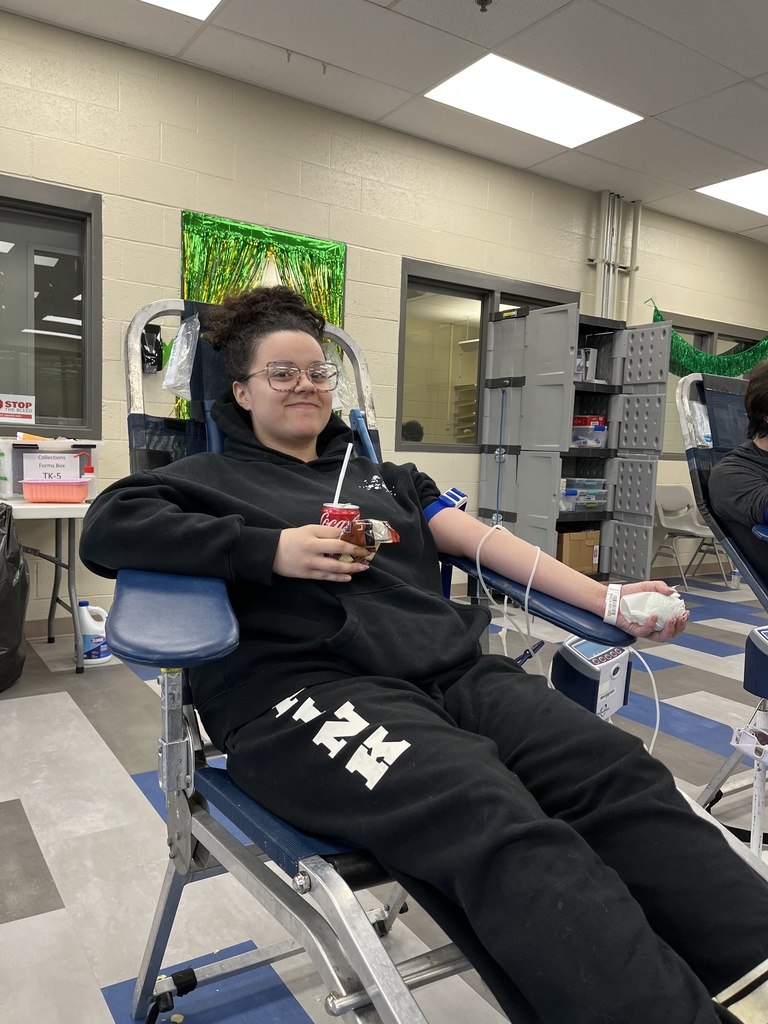 Student donor sits in a blood donation chair during the campus blood drive, holding a soda and snack while the blood collection machine is connected to their arm.