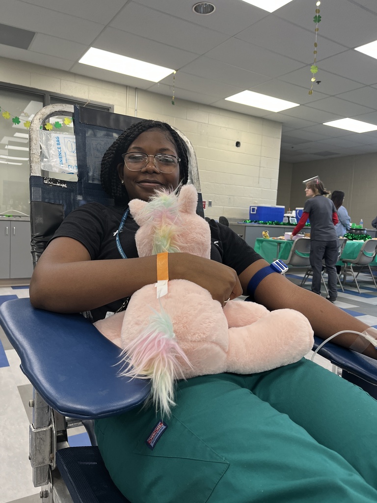 Student donor seated in a blood donation chair hugs a plush unicorn while donating blood during the campus blood drive.