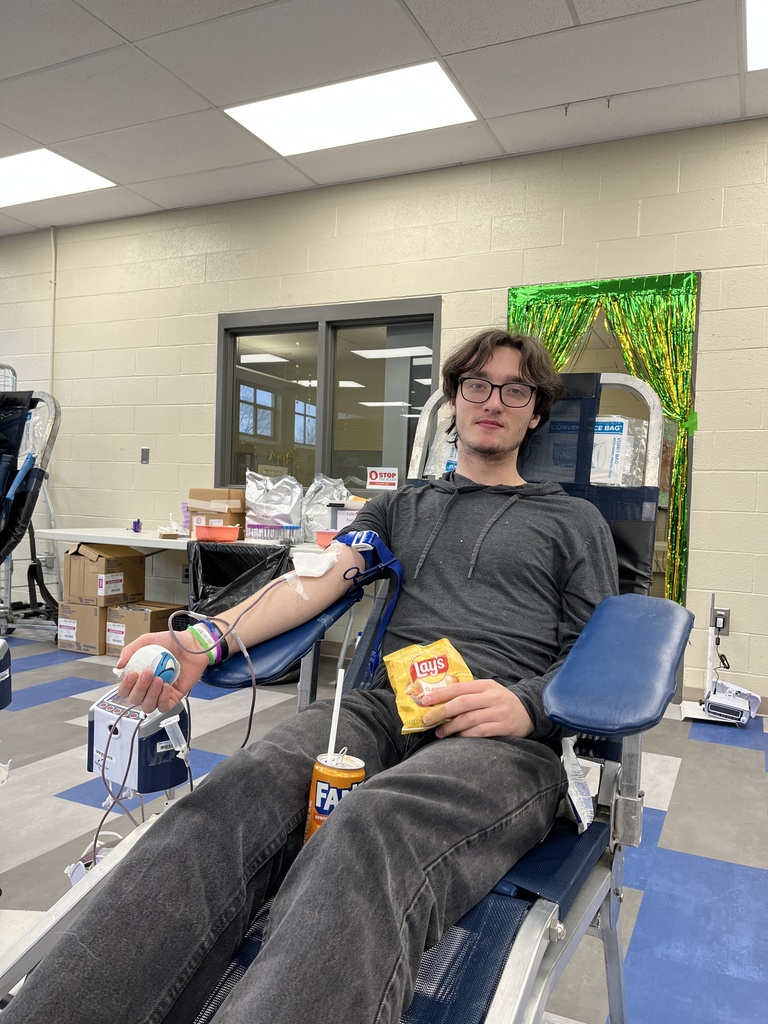 Student donor relaxes in a reclining chair while donating blood during the BCTC St. Patrick’s Day blood drive, holding a snack and drink.