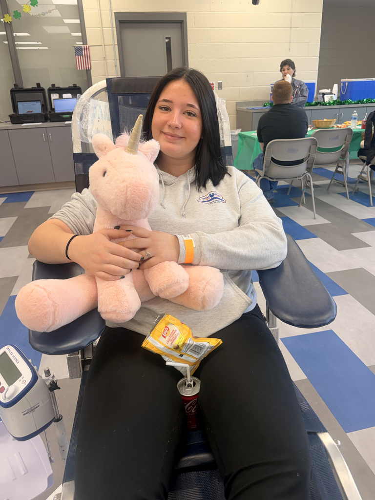 Student donor seated in a blood donation chair holds a welcome card and plush cow after giving blood during the Miller-Keystone blood drive.