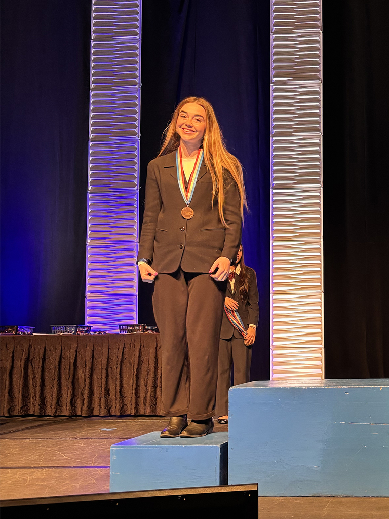 Student wearing a medal smiles while standing on a stage podium during the Penn HOSA State Leadership Conference awards ceremony.