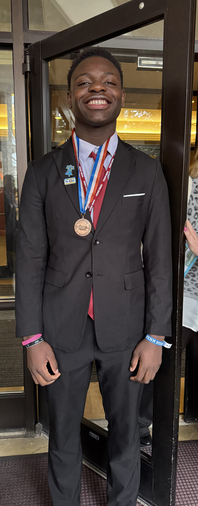Student wearing a medal and professional attire smiles while standing in a doorway during the Penn HOSA State Leadership Conference.