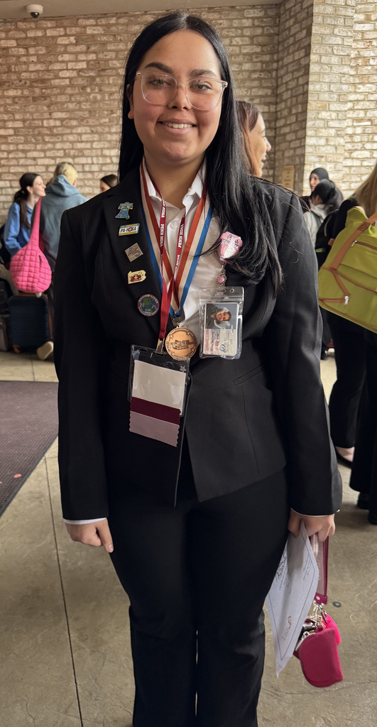 Student in professional attire wearing a medal and HOSA pins stands indoors during the Penn HOSA State Leadership Conference.