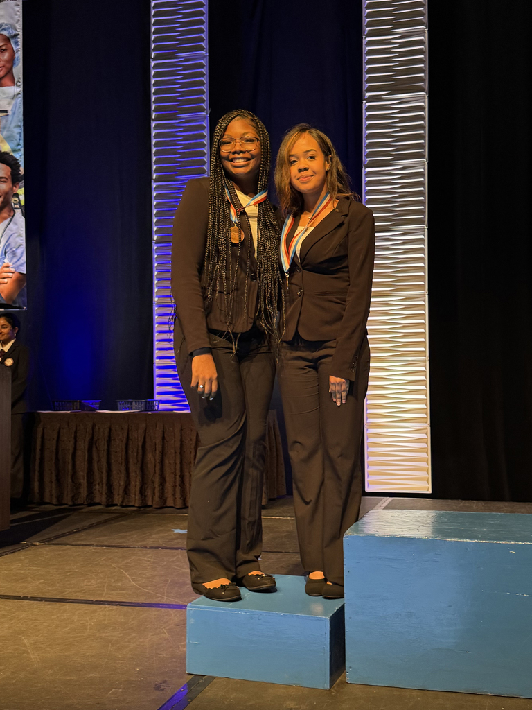 Two students wearing medals stand together on a stage podium during the Penn HOSA State Leadership Conference awards ceremony.