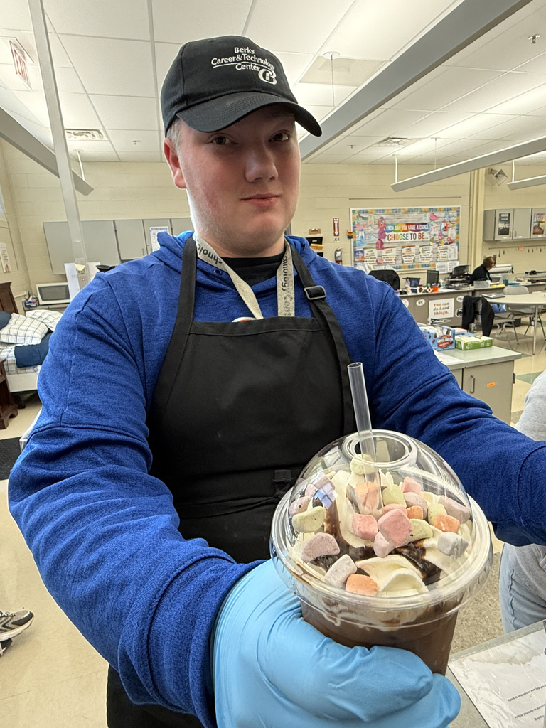 BCTC Services Occupations student wearing gloves and an apron holds a festive iced drink topped with whipped cream, chocolate drizzle, and Lucky Charms cereal.