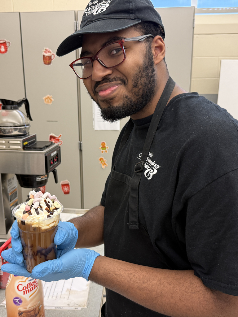 BCTC Services Occupations student wearing gloves and an apron holds a festive iced drink topped with whipped cream, chocolate drizzle, and Lucky Charms cereal.