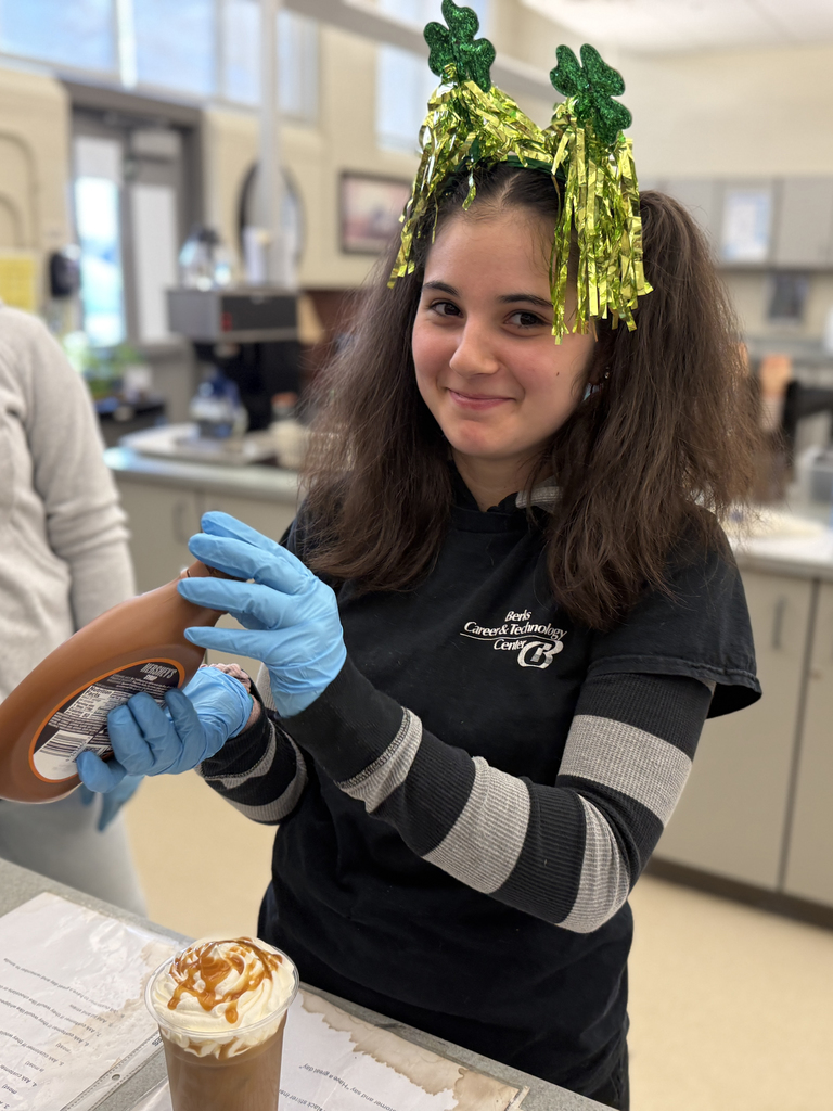 BCTC Services Occupations student wearing a shamrock headband adds caramel drizzle to a St. Patrick’s Day themed iced drink topped with whipped cream.