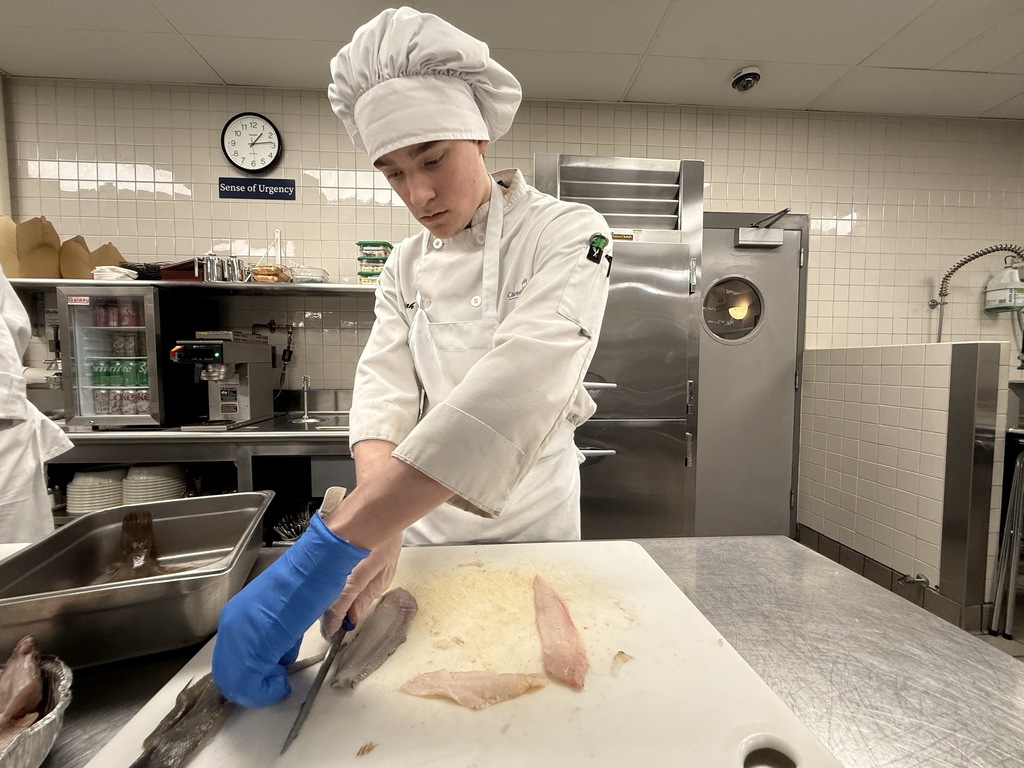 Culinary Arts student fillets a flatfish on a cutting board, separating the fillet during a seafood preparation lesson in the BCTC kitchen.
