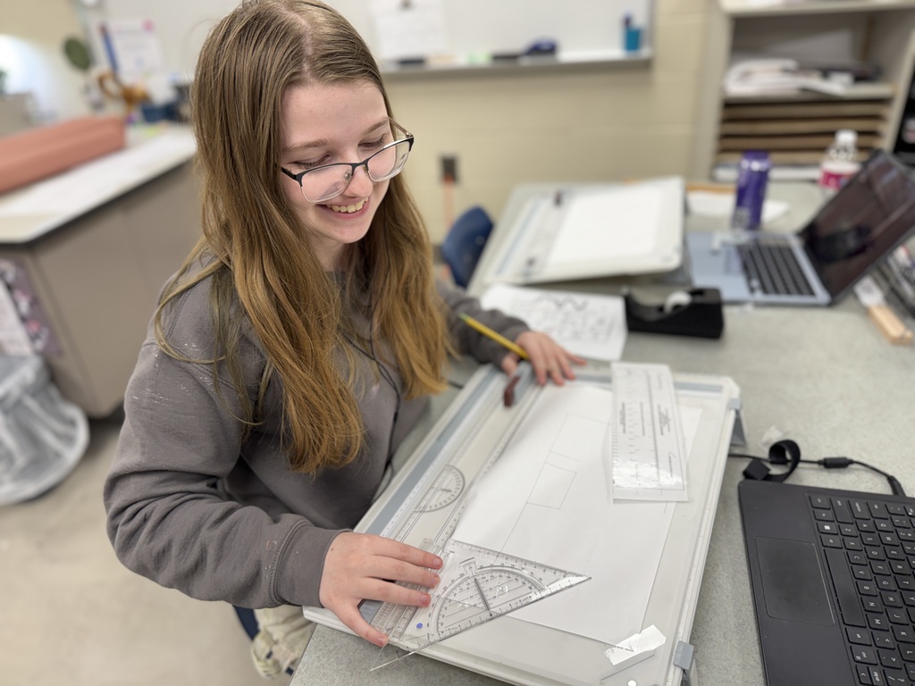 Student uses a ruler and protractor on a drafting board to create a floor plan design during a classroom activity.