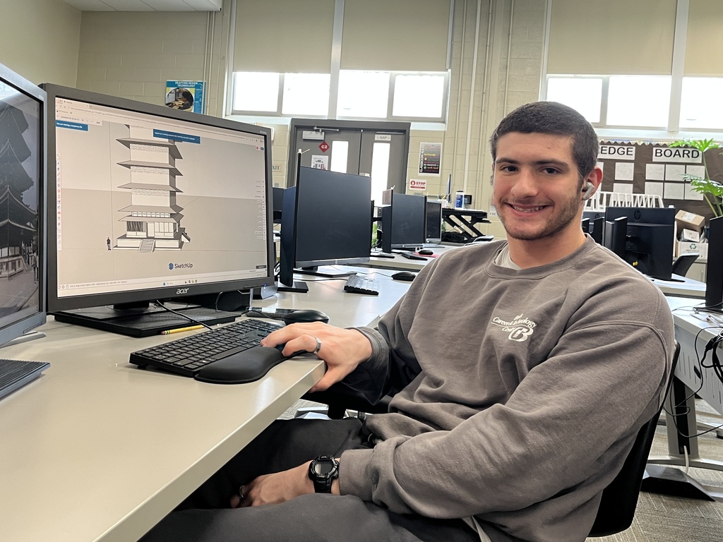 Student seated at computer creating a multi-story building model in SketchUp in a drafting classroom.