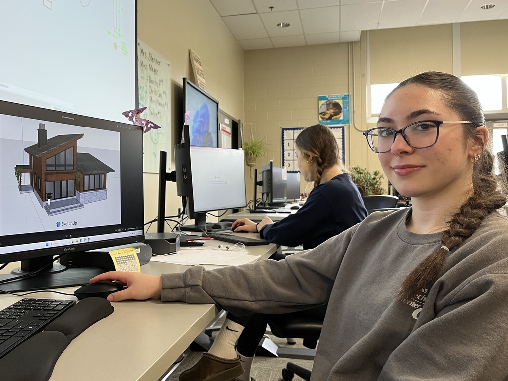 Student at computer working on a 3D home rendering in SketchUp, with classmates working at nearby stations.
