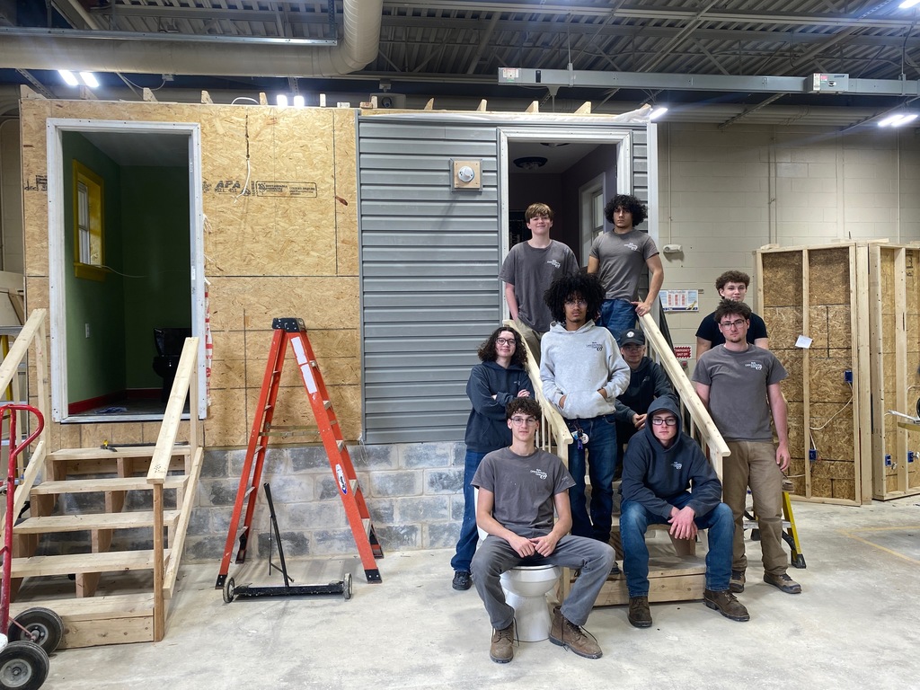 Group of Building Construction Occupations students pose on and around the partially dismantled training structure in the shop.