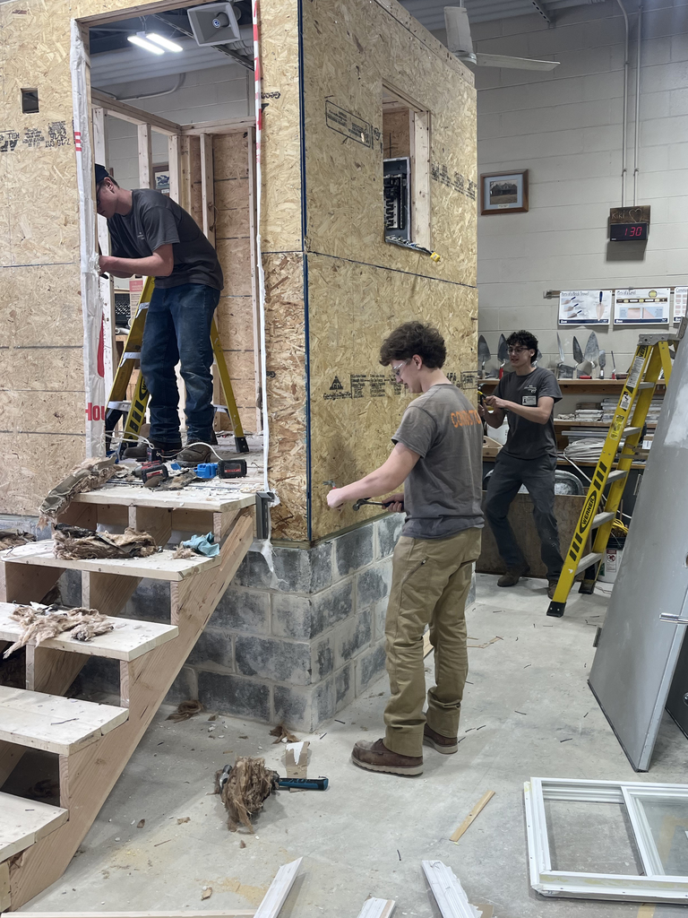 Students use hammers and tools to remove siding and framing from the training structure inside the construction lab.