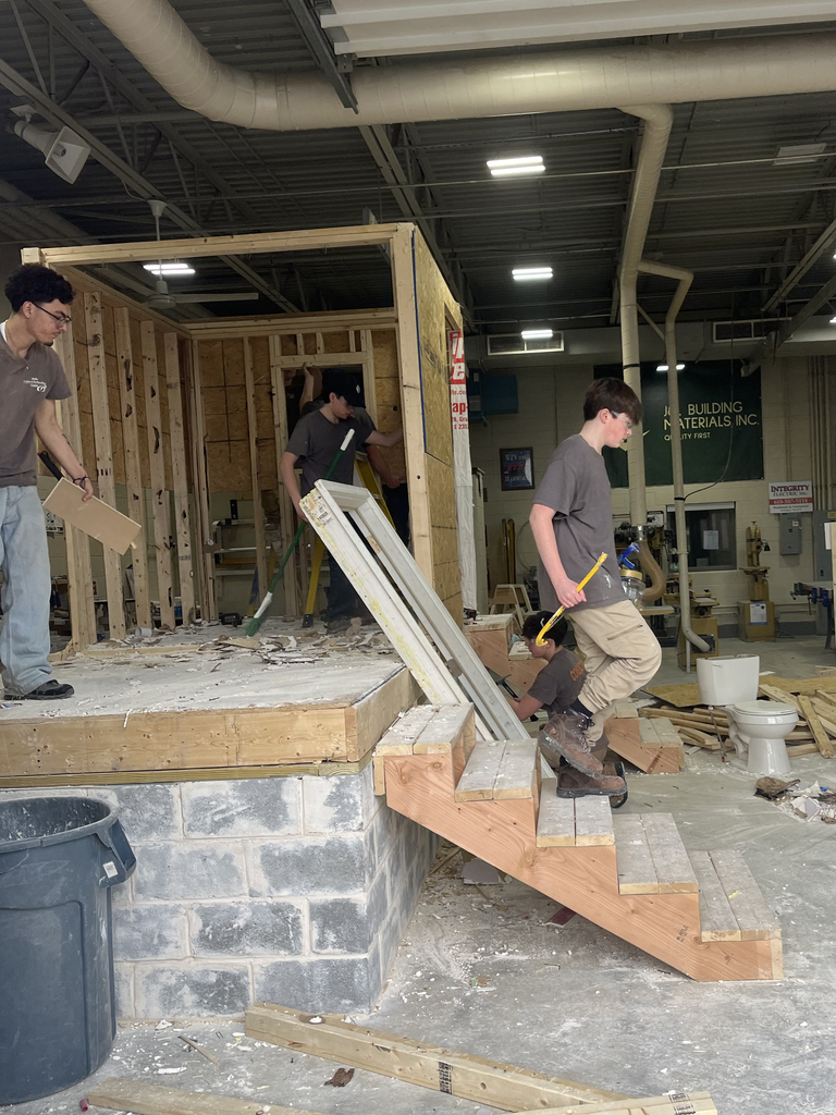 Student steps down from the structure holding a hammer while others continue demolition and cleanup in the background.
