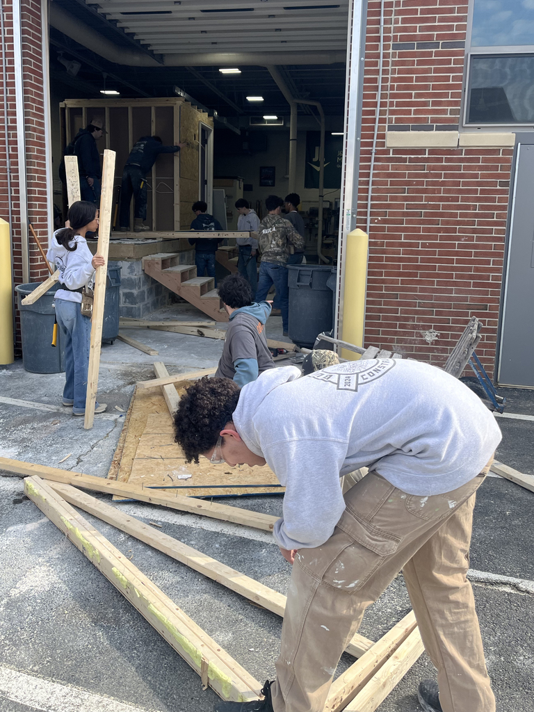 Students carry and sort wood debris outside the shop as part of dismantling the training structure.