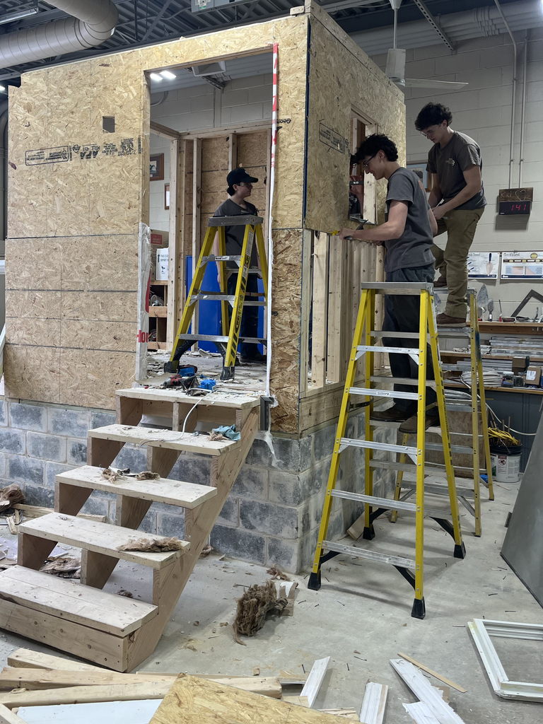Students work together removing wall panels and structural pieces from the training structure using ladders and hand tools.