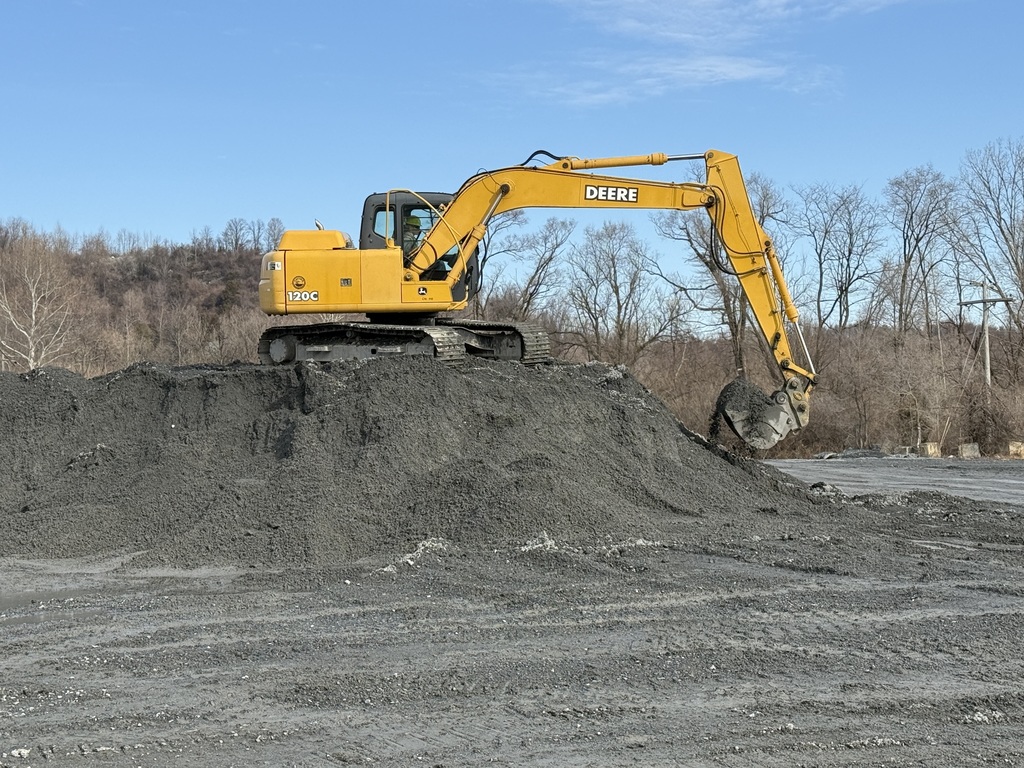 Excavator moves a load of gravel from the top of a mound at a quarry.