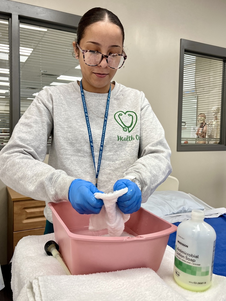 Student wearing gloves washes cloths in a basin with antimicrobial soap during a healthcare skills lab.