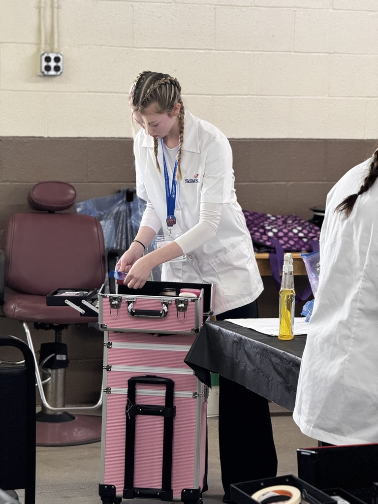 Student in a white lab coat organizes tools and supplies at a workstation during a healthcare-related competition.